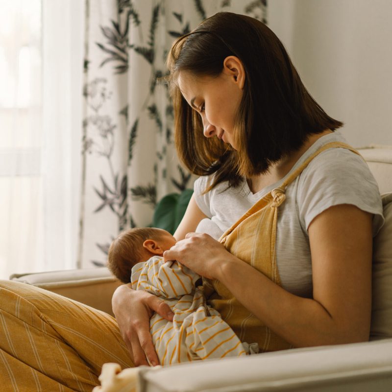 Newborn baby boy sucking milk from mothers breast. Portrait of mom and breastfeeding baby. Concept of healthy and natural baby breastfeeding nutrition.